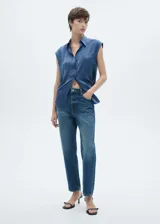 Camisa azul sin mangas de tejido fluido y satinado, con cuello camisero, cierre frontal con botones y bolsillo de parche en el pecho.