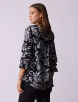 Blusa negra con estampado floral blanco, cuello mao con escote en V y abertura frontal con botones. Manga 3/4 con terminación fruncida.