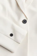 Blazer entallado color blanco, con solapas de muesca y cierre de un botón. Bolsillos de adelante ribeteados, botones decorativos en los puños y abertura atrás.