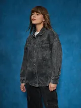 Sobrecamisa negra de denim con cuello clásico, cierre frontal con botones a presión, mangas largas con puños abotonados, dos bolsillos con solapa en el pecho y corte holgado.