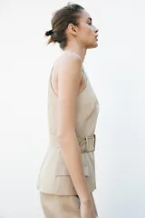 Vestido midi color beige con cuello halter cruzado, cinturón con hebilla y bolsillos tipo parche.