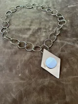 Collar plateado con cadena de eslabones ovalados y redondos. Dije en forma de rombo con círculo de nácar en el centro.