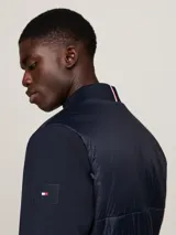 Campera bomber azul marino con mangas largas, cuello, puños y bajo acanalados. Presenta cierre frontal con cremallera, dos bolsillos laterales y logo de Tommy Hilfiger bordado en el pecho.