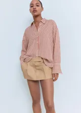 Camisa de manga larga con cuello camisero y cierre frontal de botones. Diseño recto con estampado de rayas verticales en tonos rojizos y beige.