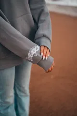 Hoodie gris con capucha y cordones ajustables, de corte holgado y manga larga. Presenta un bordado de flores blancas en la espalda y un pequeño bordado en la manga.