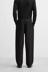 Pantalón negro de corte amplio, con pliegues frontales, bolsillos laterales y traseros de ojal. Incluye cinturón de la misma tela con hebilla metálica.