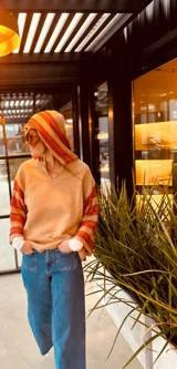 Sweater beige con capucha y mangas largas tejidas con rayas horizontales rojas y amarillas.