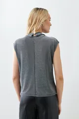 Blusa plateada de lurex con cuello alto y tablas en los hombros. Sin mangas.