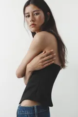 Top bustier negro sin mangas, con escote recto y bajo asimétrico. Cierre lateral con cremallera oculta.