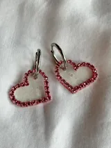 Par de aros colgantes con forma de corazón, con borde de strass rojos y aro superior plateado.