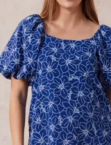 Blusa azul con estampado floral blanco, cuello cuadrado, mangas cortas abullonadas y frunce en los hombros.