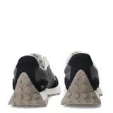 Championes New Balance modelo 327, con capellada en tonos negro, gris oscuro y gris claro. Presenta el logo 'N' sobredimensionado en gris claro y cordones blancos. La suela es gruesa, de color blanco con detalles en goma gris/tostada en la punta y el talón.