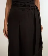 Pantalón pantalona de sastrería color negro, confeccionado en tejido texturizado. Presenta corte amplio, superposición lateral con lazo y tiro alto.