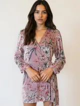 Vestido corto rosado con estampado floral, escote cruzado, mangas largas y lazo en la cintura.