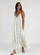 Vestido largo color crudo, con breteles finos, escote en V y volados verticales en el frente.