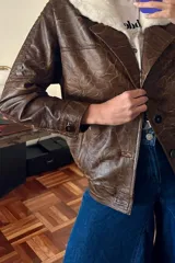 Campera bomber de cuero marrón veteado con cuello desmontable de corderito crudo y detalle de pasamanería en las mangas.