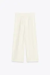 Pantalón culotte color crudo, de tiro medio, confeccionado en lino. Presenta bolsillos laterales, pinzas delanteras, pierna ancha y cierre frontal con cremallera, botón y ganchos metálicos.