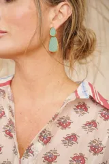 Aros colgantes con forma abstracta, color verde agua con borde dorado.