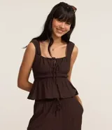 Blusa blanca con breteles anchos y escote cuadrado, detalle de lazo ajustable en el centro del busto y volado en el ruedo. El tejido es texturizado y ligero.