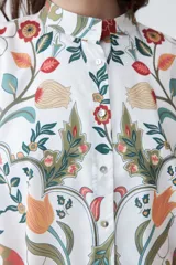 Camisa oversized con estampa floral en tonos naranja, verde y rojo sobre fondo blanco, con cuello clásico y cierre frontal con botones.