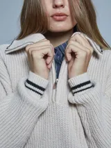 Sweater color crema de tejido grueso con medio cierre, cuello alto y detalles deportivos con rayas negras en puños y hombros.