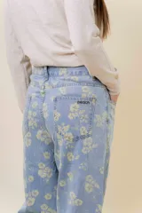 Pantalón de jean de tiro medio-alto, pierna ancha y lavado celeste claro, con estampado floral en tono amarillo pálido.