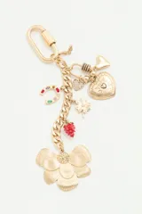 Llavero dorado con cadena de eslabones y múltiples dijes colgantes, incluyendo una flor grande texturizada, una frutilla roja, una herradura con piedras de colores, un trébol de cuatro hojas, un corazón con cristales y un corazón grabado. Cuenta con un cierre de mosquetón grande.
