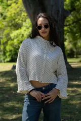 Camisa crop de muselina color blanco con lunares negros, corte amplio, cuello con volados y botones frontales.