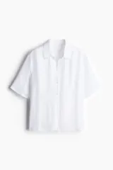 Camisa blanca de viscosa con efecto arrugado, de manga corta, corte holgado, cuello clásico, botones frontales y canesú con pliegue de caja en la espalda.