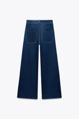 Pantalón de jean de tiro alto color negro con pierna ancha, bolsillos delanteros y traseros, y cierre frontal con cremallera y botón metálico.
