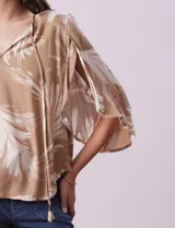 Blusa de crepe color beige con estampado de hojas blancas, cuello redondo con escote en V y lazo de ajuste, mangas 3/4 con tajo.