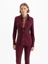 Camisa de mangas largas en viscosa color bordó, con calce relajado y bolsillos plaqué con tapa en el frente. El cuello, la cartera, los puños y el canesú están realizados en tela complemento. Los broches snap black níquel llevan el logo JCH grabado.