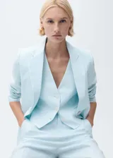 Chaqueta de lino color celeste con cuello de pico y solapas con muesca, cierre frontal con botón, manga larga con puños abotonados, diseño recto, dos bolsillos de ribete en la parte delantera y abertura posterior en el bajo.