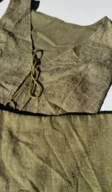 Conjunto de top y falda verde oliva con textura. El top es sin mangas, con escote en V y lazo ajustable en el centro. La falda es corta y ajustada.