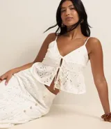 Blusa cropped blanca de algodón con bordado floral, breteles finos y escote en V con lazo frontal.