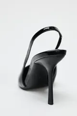 Zapato destalonado negro acharolado con tacón fino y punta. Tiene una tira trasera con elástico.