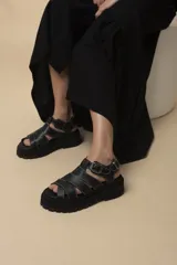 Sandalias negras de cuero con plataforma y tiras entrecruzadas con costuras blancas.