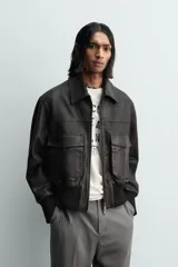 Cazadora estilo bomber cropped fit de piel negra, con cuello solapa, cierre frontal de cremallera, bolsillos frontales de plastrón con solapa y puños y bajo de rib elástico ancho.