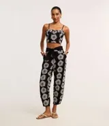 Pantalón zanahoria de cintura alta, confeccionado en laise negro con bordado floral blanco y lazo en la cintura.