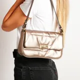 Cartera al hombro color dorado con diseño acolchado y cierre con broche metálico.