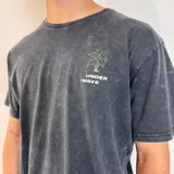 Remera gris con efecto gastado, corte clásico y estampa en la espalda con la frase "The Green House" y un dibujo de una planta oreja de elefante.