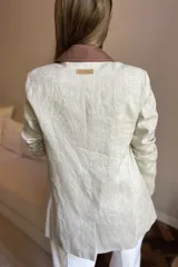 Blazer de lino color blanco con solapas y cuello en color beige, corte entallado, botón de nácar, tajo en la espalda y bolsillos laterales.