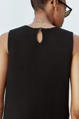Vestido corto de punto negro con panel lateral color crema, de cuello redondo y sin mangas.