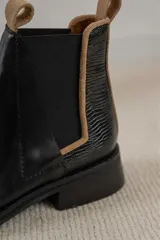 Botas Chelsea negras de cuero con elástico lateral y tirador trasero en color tostado. El talón tiene un detalle de cuero texturizado.