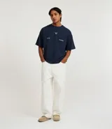 Pantalón de corte skater confeccionado en sarga de algodón color crudo, con cintura con trabillas, cordón ajustable, cierre tradicional, bolsillos y costuras contrastantes.