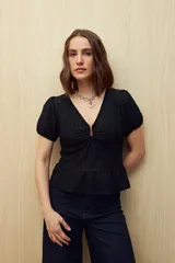 Top negro con textura tramada, escote en V con frunce central, mangas cortas con elástico y volado en el ruedo.