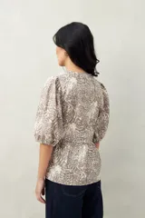 Blusa estampada color beige y blanco, con mangas abullonadas, escote redondo y lazos frontales.