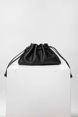 Bolso tipo sobre de cuero color rojo, con frunce superior y cierre con cordones. Tiene correa larga desmontable y bolsillo interno con cierre.