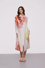 Vestido camisero midi color beige con estampado abstracto en tonos naranja, rojo, verde y amarillo. Tiene cuello camisero, mangas largas con puños abotonados y cierre frontal con botones.