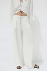 Pantalón blanco de lino, de corte ancho, tiro medio, con trabillas y cintura elástica ajustable con cordones.
